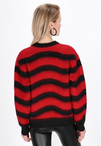Maglione over-size a righe rosse e nere con una trama morbida, scollatura rotonda e polsini a coste. Presenta strisce ondulate in tutto il capo.