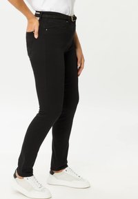 Jeans skinny neri con una texture liscia, dotati di una cintura in vita e tasche anteriori. Abbinati a sneakers bianche e a una maglietta casual.