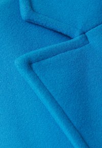 Tessuto di un brillante blu con una superficie testurizzata che mostra bordi sovrapposti e contorni morbidi. Il materiale sembra soffice, con una finitura pelosa e senza motivi visibili.