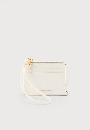 Porte-cartes en cuir blanc avec fermeture éclair dorée, bracelet pour poignet et logo Michael Kors sur la poche avant, sur fond uni.