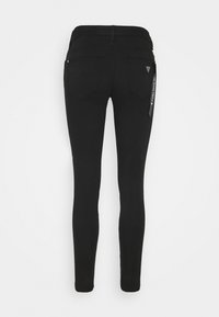 Zwarte stretchjeans met een aansluitende pasvorm, voorzien van twee achterzakken en een label aan de zijkant. Gladde textuur met een naadloos ontwerp.