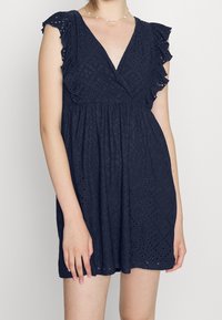 Navy sininen mekko, jossa on röyhelöhihoja, V-pääntie ja tekstuurikangas, jossa on reikäkuvioita. Rennon mallinen, jossa on kerrosselkä.