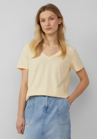 V-hals t-shirt met korte mouwen in lichtgele katoenstof, relaxed fit, gladde textuur, gecombineerd met een denim rok.