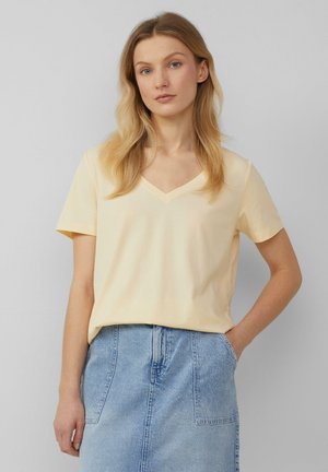 V-neck short-sleeve t-shirt in light yellow cotton fabric, relaxed fit, smooth texture, paired with a denim skirt.