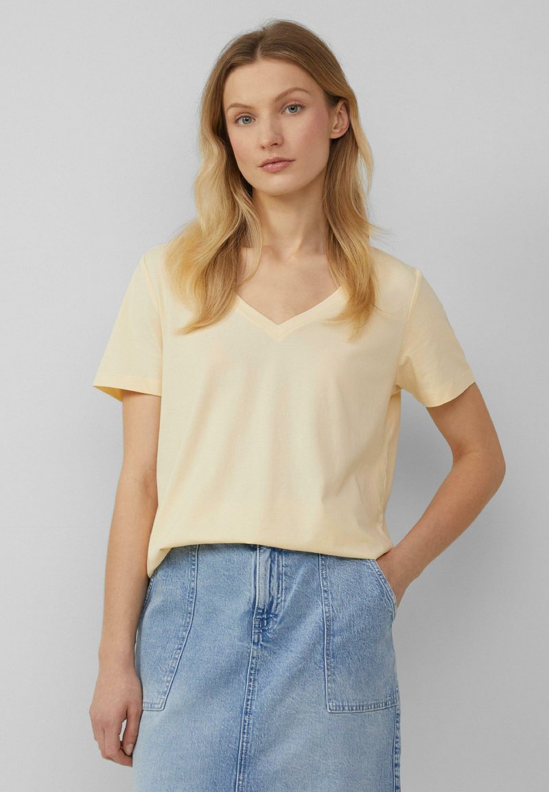 V-hals t-shirt met korte mouwen in lichtgele katoenstof, relaxed fit, gladde textuur, gecombineerd met een denim rok.