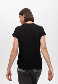 Black short-sleeve top with a round neckline and a relaxed fit, featuring a smooth texture and subtle side slits.