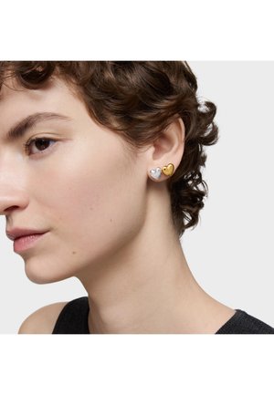 Orecchini a forma di cuore in metallo argento e oro, con finiture lisce e colori a contrasto, indossati all'orecchio di un modello.