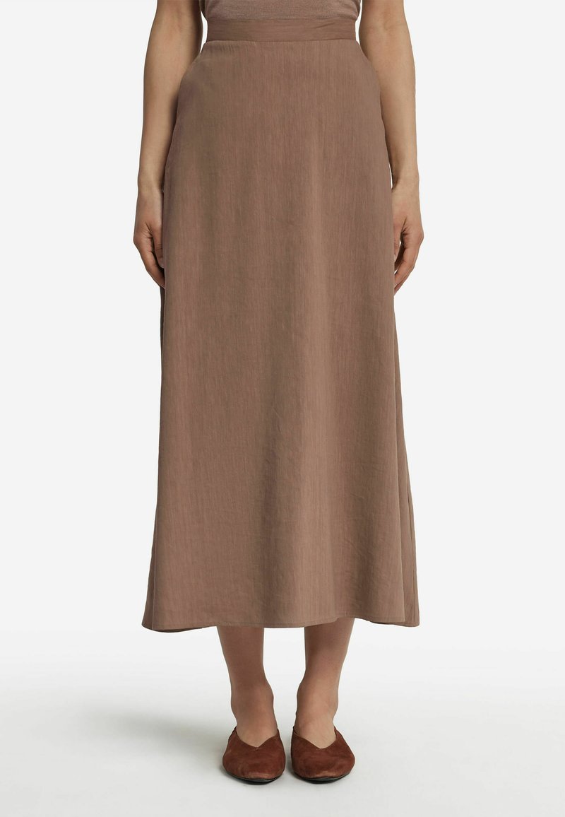 Jupe brune mi-longue en tissu texturé avec une taille lisse. Associée à des chaussures plates marron foncé.