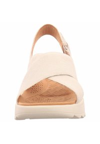 Sandale de couleur claire avec un dessus texturé, des brides croisées et une semelle intérieure rembourrée. La semelle est légèrement surélevée avec des détails antidérapants.