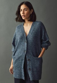 Mörkblå knäppbar cardigan i texturerad stickad tyg med oversize fickor och avslappnade ärmar.