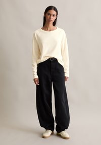 Cream long-sleeve shirt, relaxed fit, black wide-leg pants, minimal design, textured fabric, paired with white sneakers, simple black belt.