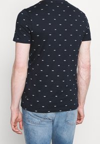 Marineblaues T-Shirt aus Baumwolle mit kleinen weißen Bootmustern, kurzen Ärmeln und Rundhalsausschnitt.