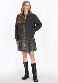 Fekete farmer bomber dzseki bordázott hemmel, sötétzöld virágmintás ruha felett. Térdig érő fekete bőr csizmák csatokkal.