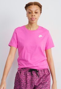 Rožinė medvilninė marškinė su apvalia apykakle ir trumpomis rankovėmis, puošti mažu baltu Nike logotipu, suderinti su rožiniais leopardų rašto šortais.