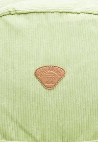 Groene geribbelde stof met een leren patch met structuur, featuring een logo. De patch is driehoekig en bruin, geplaatst nabij het midden.