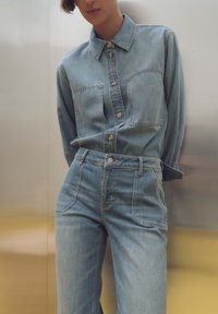 Camicia di jeans azzurro chiaro con due tasche sul petto, chiusura a bottoni e colletto. Abbinata a jeans a vita alta in tonalità azzurro chiaro.