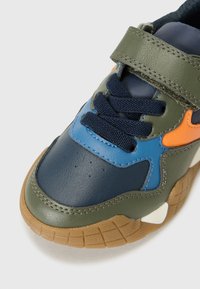 Baskets en cuir avec des accents bleu foncé, vert olive et orange. Bout arrondi, semelle en caoutchouc texturée et fermeture à lacets avec bande velcro.