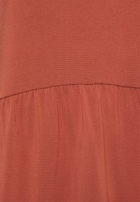 Um tecido de cor ferrugem com uma textura suave apresenta uma costura franzida na parte inferior, exibindo um drapeado sutil e um design leve.