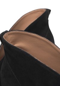 Crne antilop čizme do članaka s glatkim, svijetlosmešnim unutrašnjim dijelom od kože. Imaju špicasti otvor i prošivene detalje duž rubova.