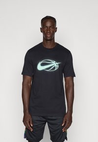 Černé tričko s krátkým rukávem s logem Nike basketbalu v světle modré barvě na přední straně. Standardní design s kulatým výstřihem, hladká textilie.