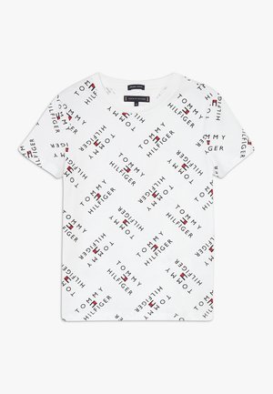 T-shirt blanc à manches courtes avec un texte "Tommy Hilfiger" répétitif en diagonale et de petits logos de drapeaux rouges, blancs et bleus partout.