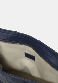 Bolso de piel azul marino con un exterior suave. El interior cuenta con un forro beige, cremalleras y una etiqueta de marca. Forma limpia y estructurada.