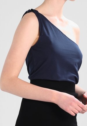 Marineblauwe top met één schouder, gemaakt van zachte stof. Voorzien van een knoopdetail aan de band. Gecombineerd met een zwarte, hooggetailleerde rok voor een aansluitende look.