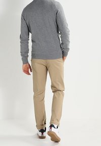 Grå stickad tröja med långa ärmar, beige slim-fit byxor och vita sneakers med röda och blå detaljer.