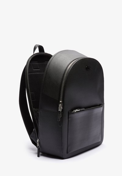 Sac à dos noir en matériau texturé avec un haut arrondi, poche zippée à l'avant et bretelles réglables. Présente un petit logo à l'avant.