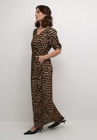 Maxi haljina s leopard uzorkom, V-izrezom, kratkim puf rukavima i bočnim džepovima, napravljena od lagane tkanine. Nosi se uz crne cipele s šiljastim vrhom.