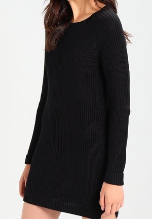 Black knitted sweater dress with long sleeves, ribbed texture, round neckline, and a loose fit. Features a slight hem at the bottom.