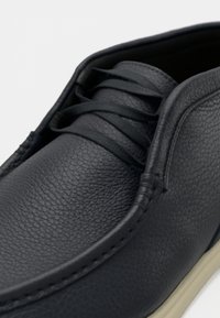 Σκούρο μπλε δερμάτινο παπούτσι με υφή, στρογγυλή μύτη και κορδόνια στο ίδιο χρώμα· η μπεζ σόλα είναι ορατή κατά μήκος της άκρης.