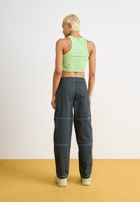 Top scurt verde cu dungi verticale, asociat cu pantaloni evazați în carouri negre. Pantalonii au cusături vizibile și buzunare laterale. Încălțăminte de culoare crem.