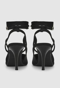 Sandali neri con tacco alto caratterizzati da un design a fasce con cavigliera avvolgente e texture in pelle liscia, con tacchi sottili e minimal hardware.