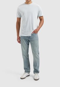 Lichtblauw T-shirt met korte mouwen, klassieke pasvorm met een ronde hals; gecombineerd met lichtblauwe spijkerbroeken en witte sportschoenen met grijze accenten.