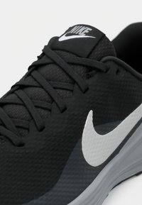 Scarpa da corsa nera con tomaia testurizzata, lacci piatti e logo Nike bianco. Include un collo imbottito e una suola in gomma resistente.