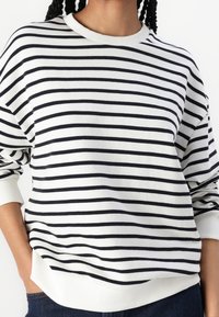 Suéter tipo pulóver a rayas en crema y azul marino, con mangas largas, cuello y puños acanalados, y un corte holgado. Tejido suave de mezcla de algodón.