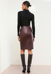 Pulover negru cu guler înalt și dungi, cu detalii cu butoane la manșete, asortat cu o fustă creion din piele ecologică de culoare bordeaux închis, de lungime până la genunchi.