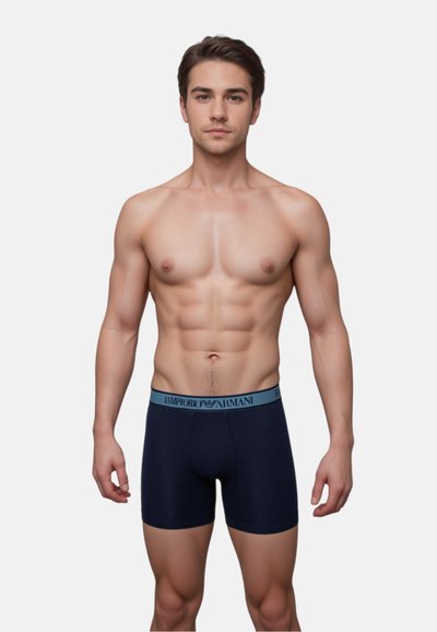 Navy boxer briefs made of soft fabric with a light blue elastic waistband featuring "Emporio Armani" logo. Fitted design, mid-thigh length.