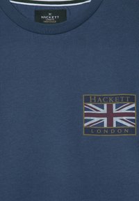 Tamno plava Hackett London Heritage majica s britanskom zastavom i Hackett London natpisom na lijevoj strani grudi.