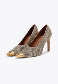 Szpilki wykonane z teksturowanej złotej i srebrnej tkaniny, z wąskim noskiem i złotą metalową nakładką. Charakteryzują się smukłą szpilką i dekoracyjnymi akcentami.