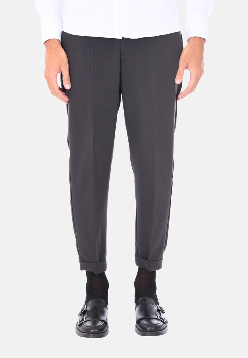 Pantaloni neri con una vestibilità sartoriale, texture subtile, orli arrotolati e linee pulite, abbinati a scarpe slip-on nere e calzini scuri.