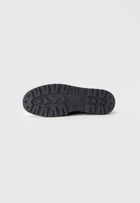 Črna gumijasta podplat čevlja z vzorčastim, strukturovanim profilom. Videlni so izraziti trikotni in krožni vzorci za oprijem. Gladki robovi in zaobljene linije.