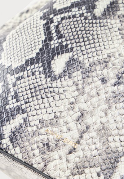 Nahaufnahme einer grauen und weißen Oberfläche mit Schlangenlederstruktur, dezentem schwarzem Muster und kleinem goldfarbenem "SIMONE BING" Logo, geprägt.