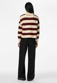 Svītrains džemperis bēšā un sarkanā krāsā, ar garām piedurknēm, ribota faktūra; kopā ar melnām bikšu platām kājām ar smalkām svītrām.