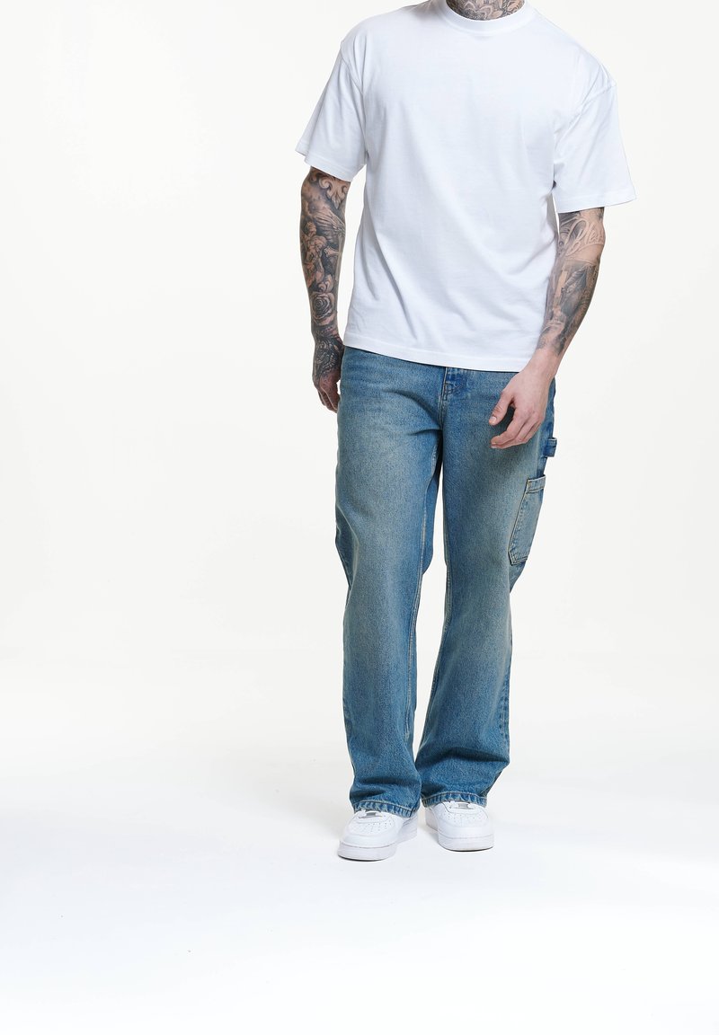 Vit bomull t-shirt i kombination med blå denimjeans med sidficka. Jeansen har raka ben, ljus tvätt och synliga sömmar.