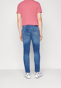 Slim-fit blå jeans i denim, med sydda bakfickor och bälteshällor, kombinerat med en rosa t-shirt och vita sneakers.
