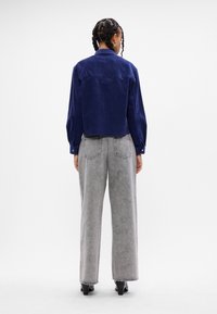 Camicetta cropped in corduroy blu navy con maniche lunghe e polsini abbottonati, abbinata a jeans larghi a vita alta grigi e scarpe nere con tacco.