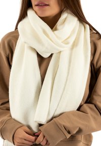 Bufanda blanca hecha de un tejido suave y texturizado, caída de manera casual alrededor del cuello, complementando un sudadera marrón.