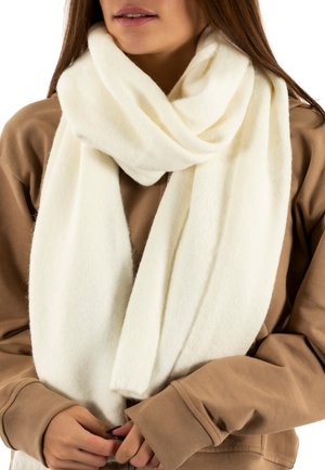 Écharpe blanche en tissu doux et texturé, drapée de manière décontractée autour du cou, complétant un sweat-shirt marron.
